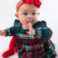 Baby in plaid dress with red bow headband.