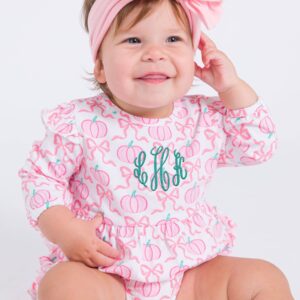 Smiling baby in pumpkin-patterned outfit with bow.
