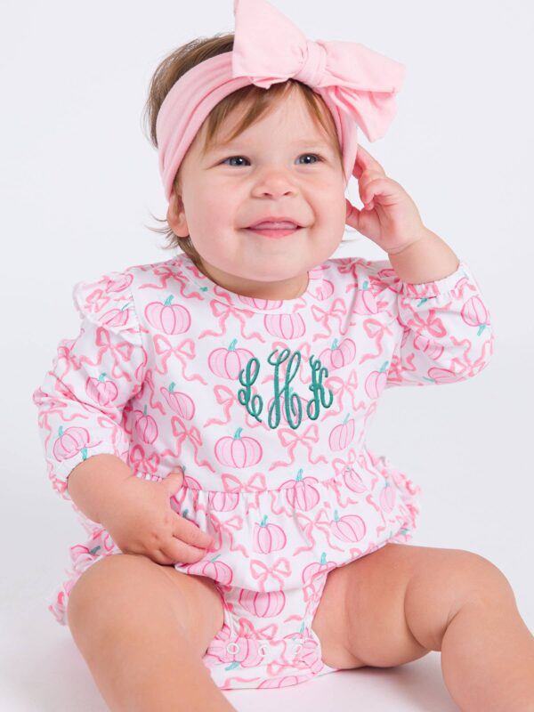 rufflebutts + ruggedbutts baby girls pink fairytale pumpkins knit long sleeve flutter bubble romper Smiling baby in pumpkin-patterned outfit with bow.