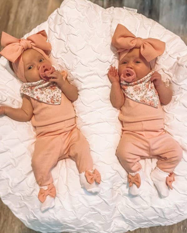 itzy ritzy sweetie soother™ pacifier sets (2 pack): pink bows Twin babies in matching outfits with pacifiers.