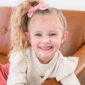 Smiling girl with pink bow and necklace.