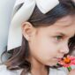 Young girl with bow, heart earring, smelling flower.