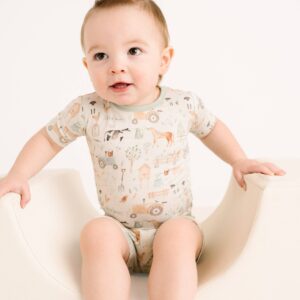 Baby wearing patterned romper on white seat.