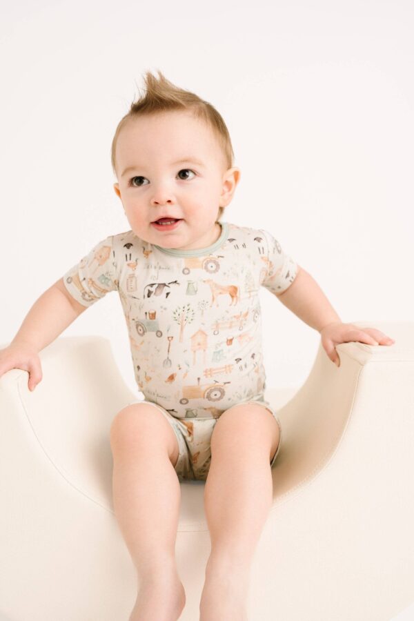 little one shop little farm bamboo shorts set Baby wearing patterned romper on white seat.