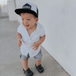 Child in white shirt and cap smiling outdoors.