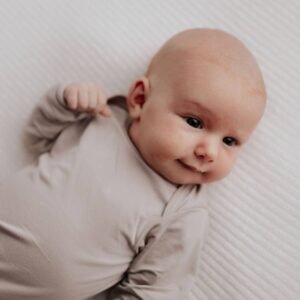 Baby lying on white textured blanket, smiling.
