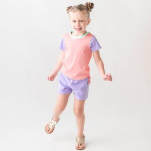 Child wearing colorful outfit and sandals, smiling.