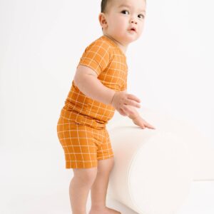 Baby in orange checkered outfit standing on ottoman