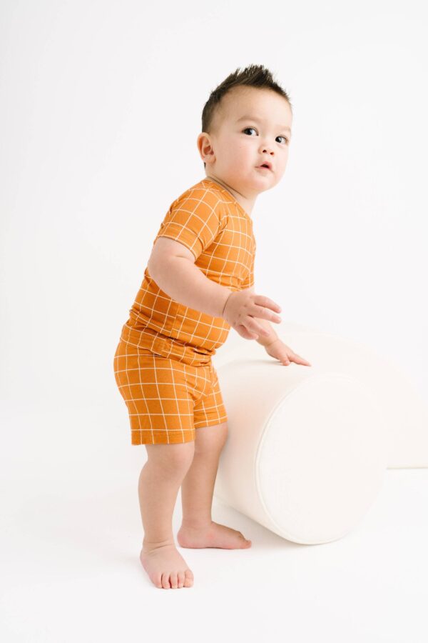 little one shop rust checks bamboo shorts set Baby in orange checkered outfit standing on ottoman