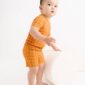 Baby in orange checkered outfit standing on ottoman