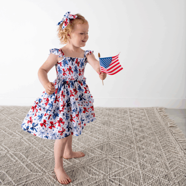 gigi and max eleanor bow clip bow 4th of july hair accessory Child holding American flag in patriotic dress.