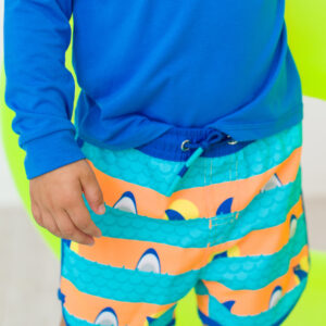 Child wearing blue shirt and colorful shark shorts.