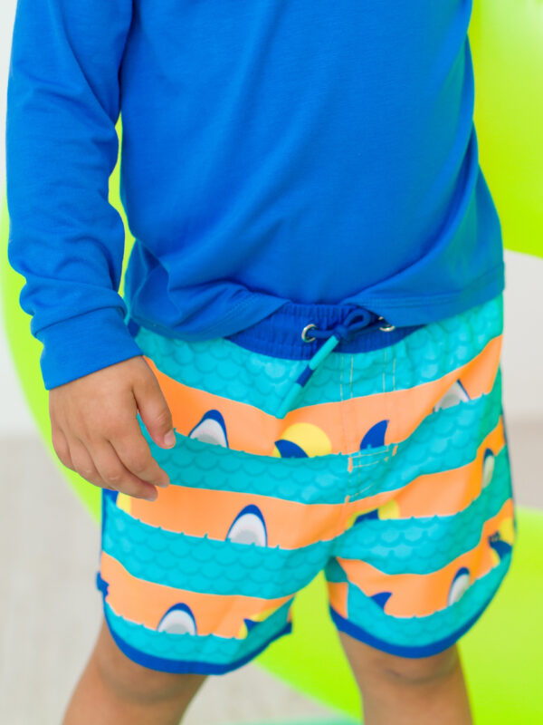 Child wearing blue shirt and colorful shark shorts.