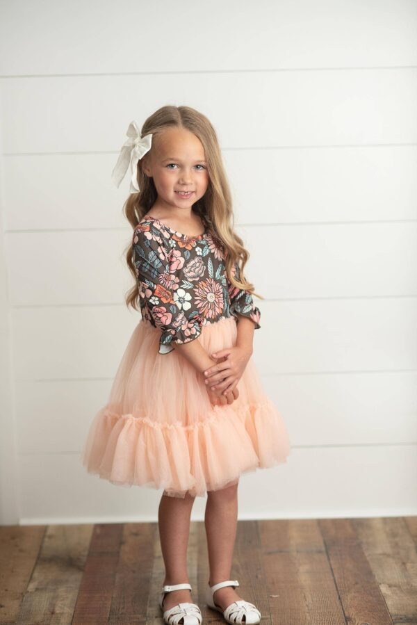 oopsie daisy kids brown & peach vintage floral tulle fall dress Young girl in floral dress, smiling indoors.