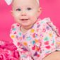 Baby wearing heart-print romper and white bow.