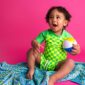 Smiling toddler holding beach ball on colorful blanket.