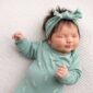 Sleeping newborn in green outfit and headband.