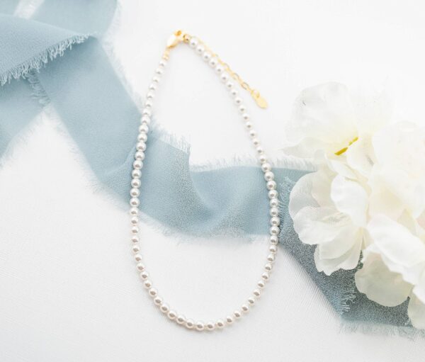 Elegant pearl necklace with blue ribbon and flowers.