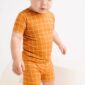 Child in orange checkered outfit on white background.