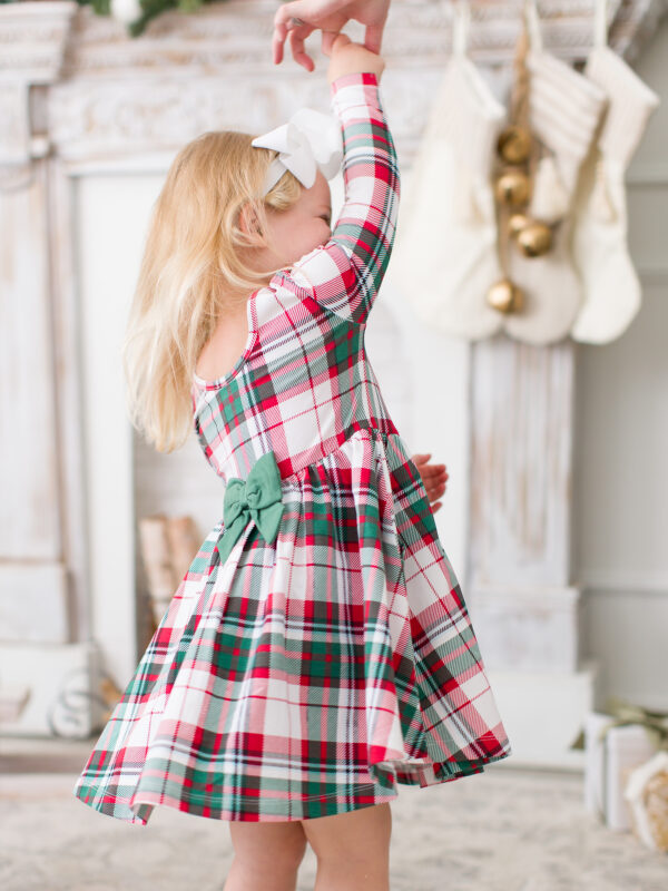 Girl in plaid dress spins in festive living room.