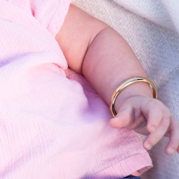 cherished moments gold classic bangle for baby & kids Baby arm with gold bracelet in pink shirt.