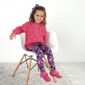 Child in pink sweater and floral leggings smiling.