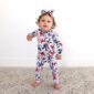 Toddler in floral onesie and headbow stands smiling.