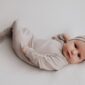 Baby in beige outfit and headband lying down.
