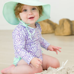 Baby with hat playing in sand indoors.