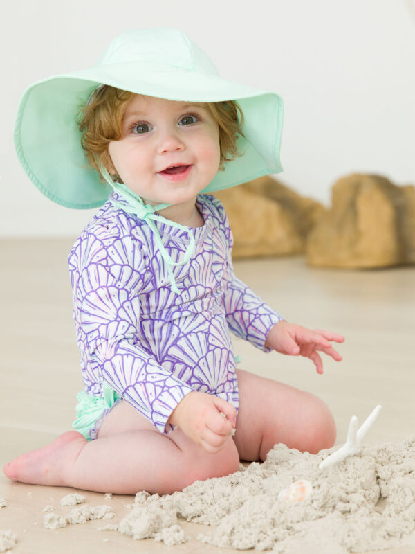 Baby with hat playing in sand indoors.