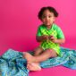 Child in checkered outfit on colorful blanket.