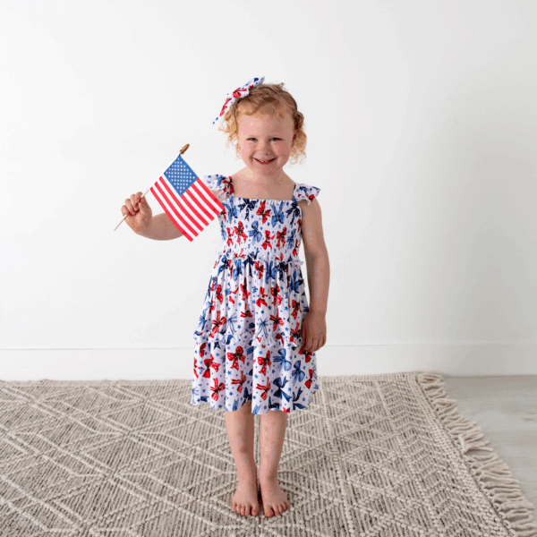 gigi and max eleanor bow clip bow 4th of july hair accessory Child holding American flag in festive dress.