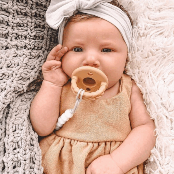 itzy ritzy sweetie soother™ pacifier sets (2 pack): agave + succulent cables Baby with pacifier and headband on blanket.