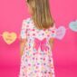 Girl in heart-print dress with bow, pink background.