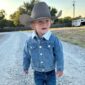 Child in cowboy hat and denim jacket outdoors.