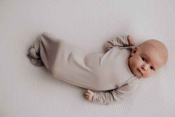 three little tots harbor mist taupe knotted gown Baby in beige sleep sack on white blanket.