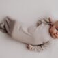 Baby in beige sleep sack on white blanket.