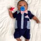 Baby with pacifier and bow tie on blanket.