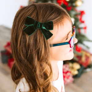 Child with glasses wearing green bow, Christmas background.