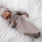 Smiling baby in gray swaddle on bed