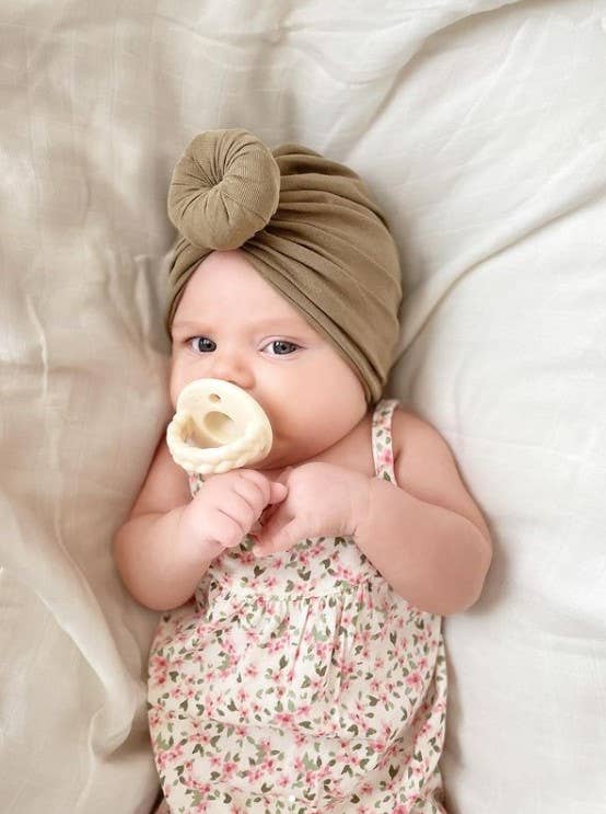 itzy ritzy sweetie soother™ pacifier sets (2 pack): toast + buttercream braids Baby with pacifier and turban on bed