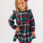 Girl in plaid dress with red bow smiling