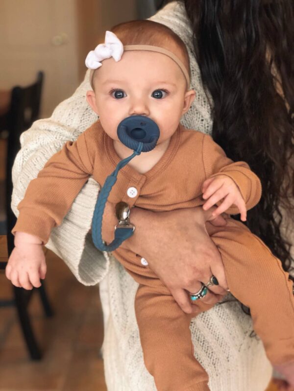 itzy ritzy sweetie soother™ pacifier sets (2 pack): agave + succulent cables Baby with pacifier and headband held by parent.