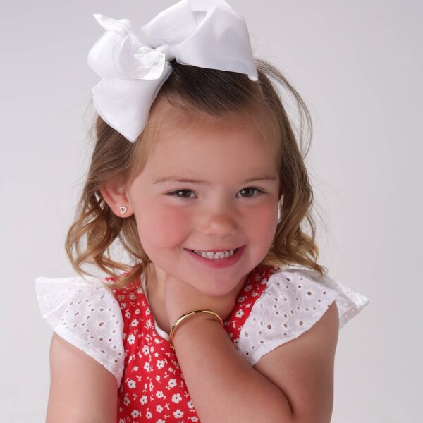 cherished moments gold classic bangle for baby & kids Smiling child with white bow and floral dress.