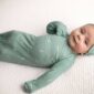 Baby in green outfit lying on bed
