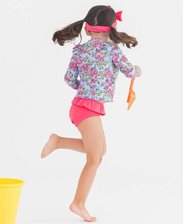 rufflebutts cheerful blossoms princess seam ruffle rash guard 2 piece Girl playing in colorful swimsuit with yellow bucket.
