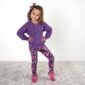 Child in purple sweater and floral leggings smiling.