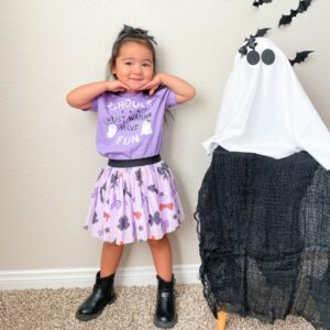 Child in Halloween costume next to ghost decoration.