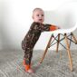 Baby in camouflage onesie standing by chair
