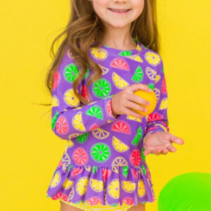 Girl in colorful citrus-patterned outfit, holding fruit.